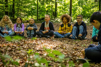 Kinder sitzen nebeneinander im Wald auf Laub