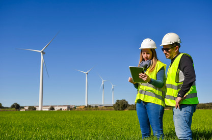 Menschen arbeiten auf Tablet im Geländer vor Windrädern