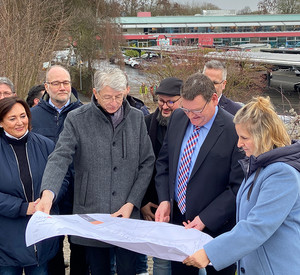 Katrin Eder, Ralf Seemann und andere schauen auf die Pläne zum Bau der PV-Anlage auf dem Parkplatz der Deichwelle