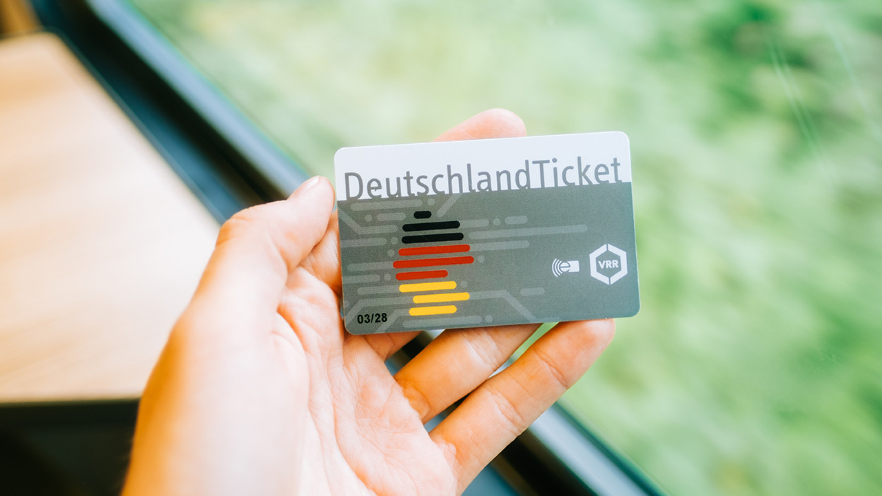 Eine Hand am Fenster eines Zugabteils hält ein Deutschland-Ticket