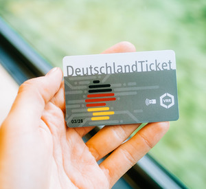 Eine Hand am Fenster eines Zugabteils hält ein Deutschland-Ticket