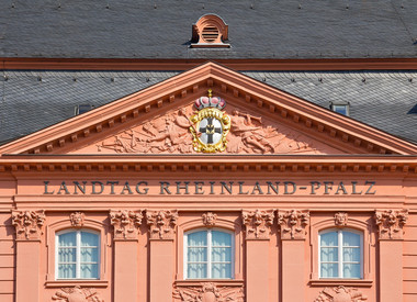 Ein rotes Gebäude mit schwarzen Ziegeln. Das Gebäude hat drei Fenster über denen "Landtag Rheinland-Pfalz" steht.  
